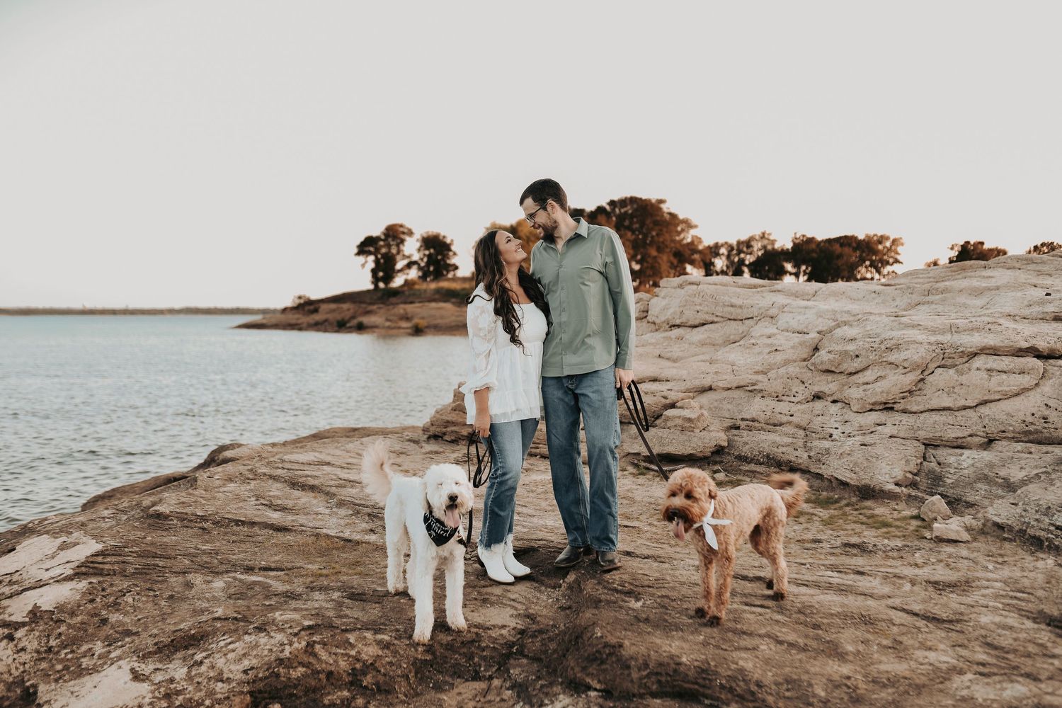a couple looks at each other and smiles as they are surrounded by their fur babies for their engagement photos on the rocks at murrell park