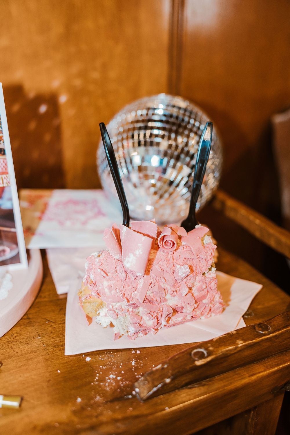 Pink buttercream cake with chocolate sticks sits on wooden table with disco ball in background.