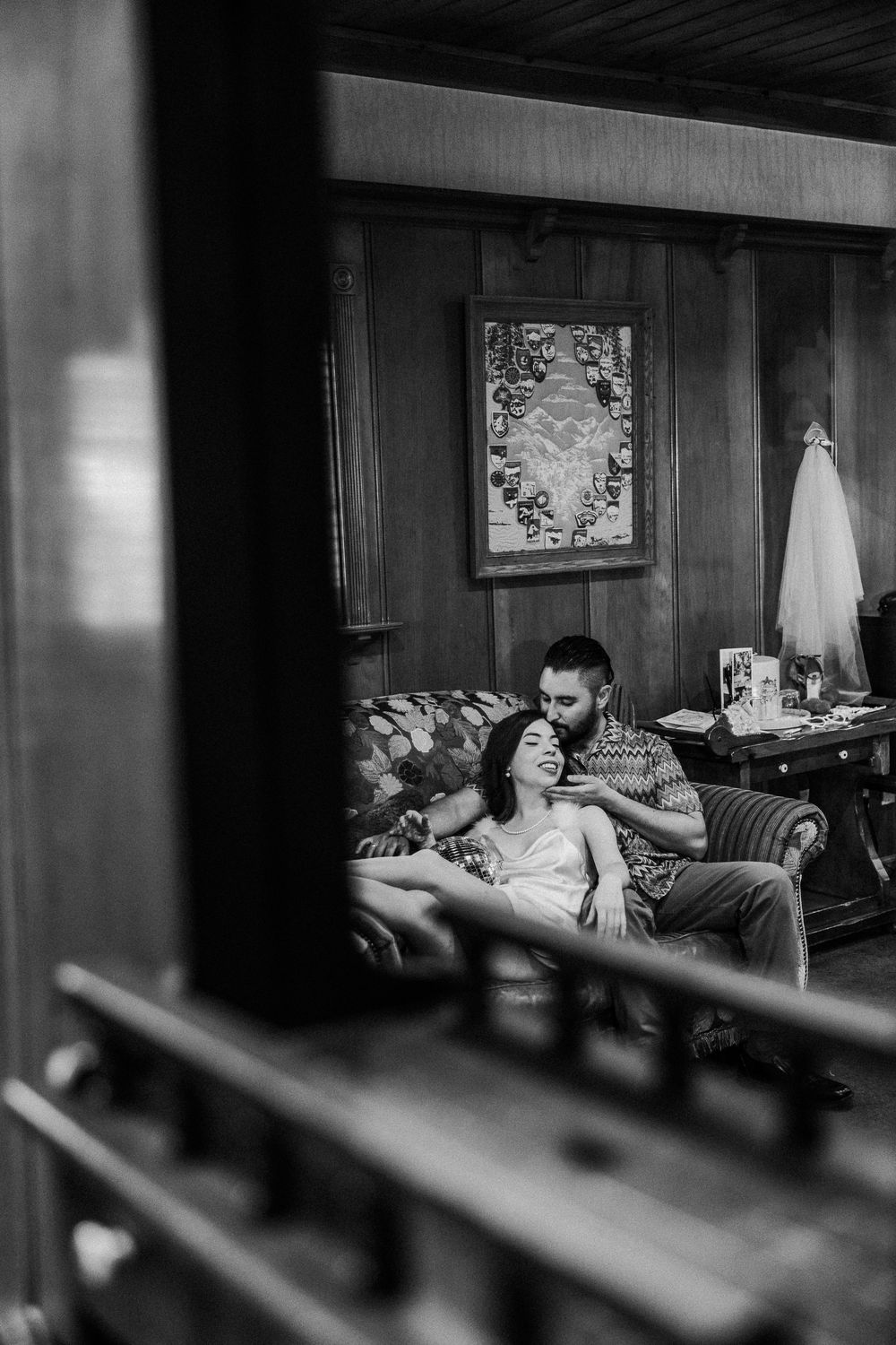 A cozy black and white photo of a couple relaxing together on a vintage leather couch in a dimly lit room.