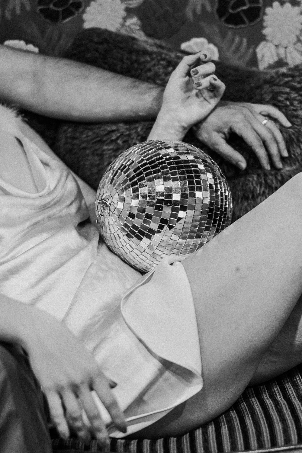 A disco ball rests on someone's lap while wearing white clothing in a black and white artistic photograph.