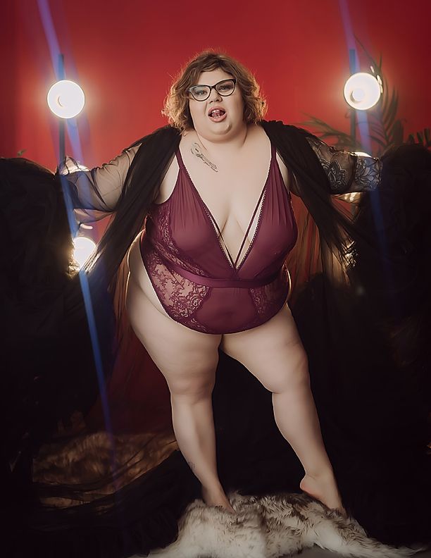 Plus size model in a burgundy bodysuit strikes a series of glamorous poses against dark moody studio lighting.