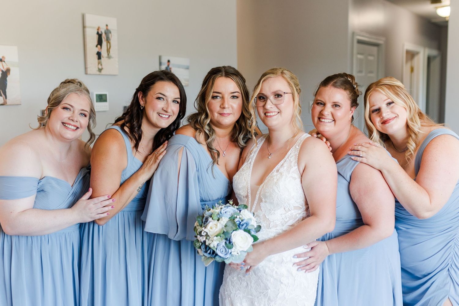 A bridal party wearing light blue bridesmaid dresses poses together with white and blue floral bouquet.