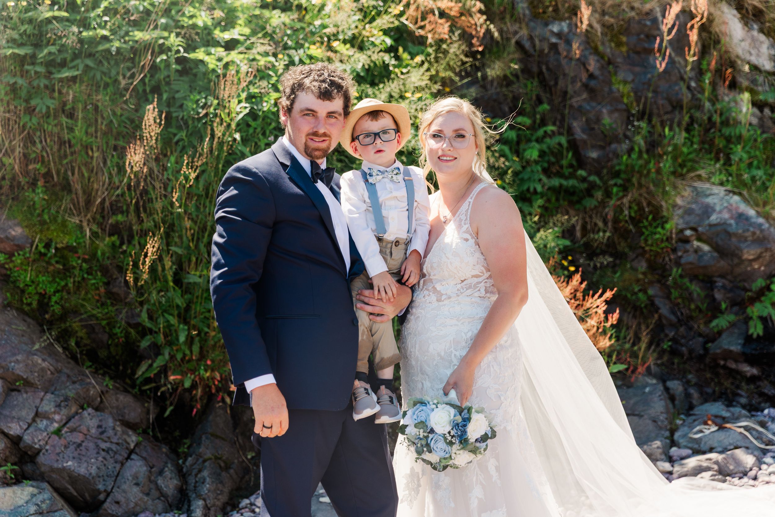 Newlyweds pose lovingly in bright sunlight among rocky terrain during outdoor wedding photo session.