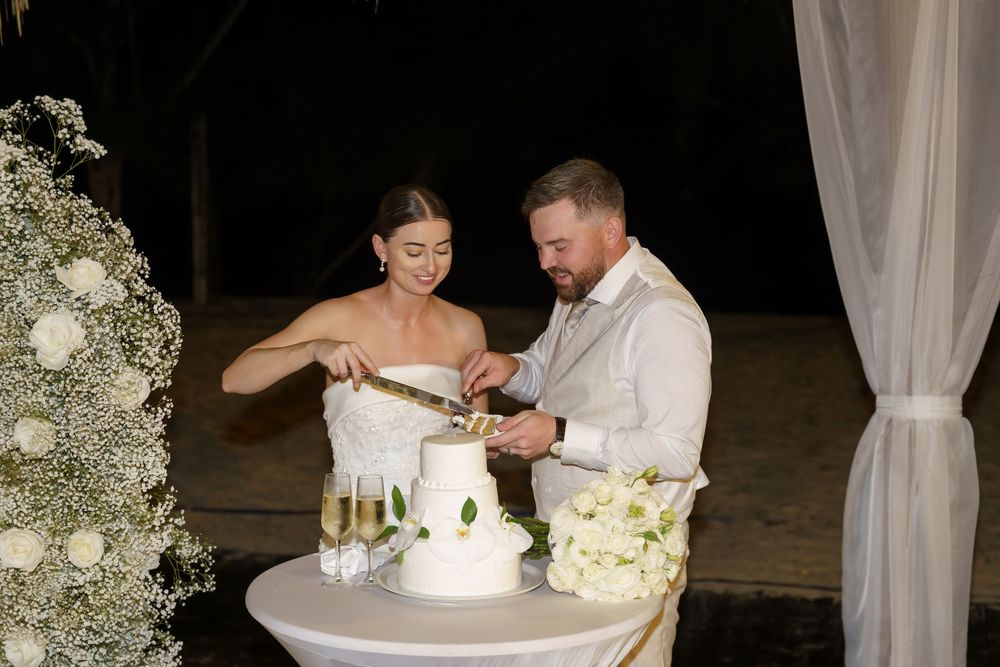 Wedding cake cutting sequence showing a couple sharing sweet moments as they cut their white multi-tiered wedding cake together.