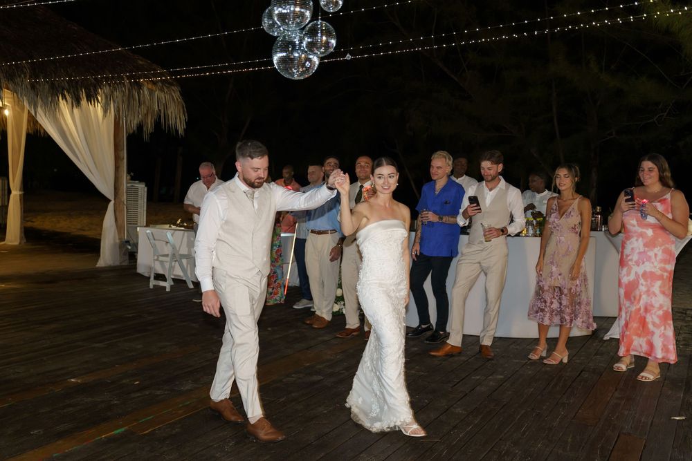 Wedding guests dance together on an outdoor wooden dance floor under a covered pavilion at an evening reception.
