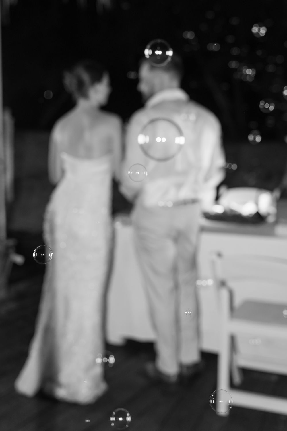 A blurry black and white photo of a couple dancing at an event with bubbles floating in the air.
