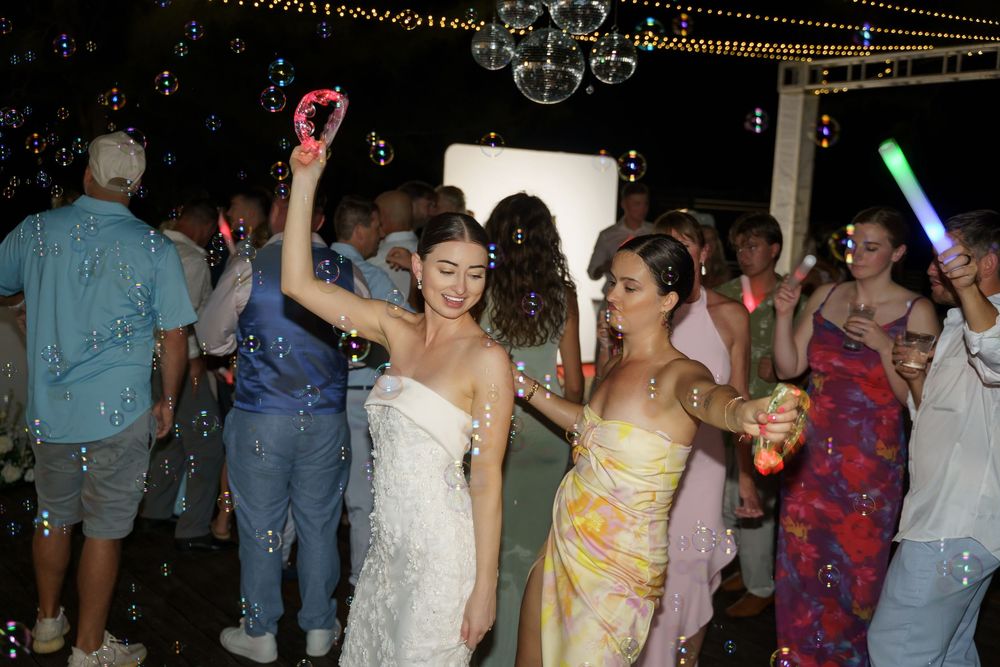 Wedding guests dance under string lights at a nighttime outdoor reception with glowsticks and festive atmosphere.
