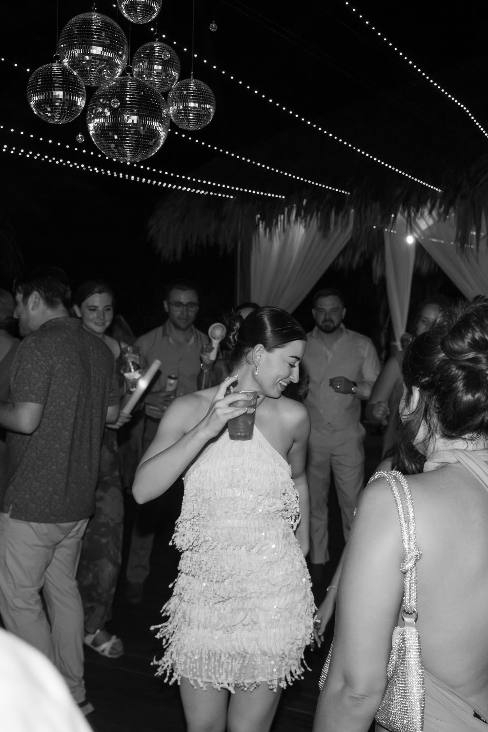 Black and white photo of people dancing under disco balls at a party with white decorative elements.
