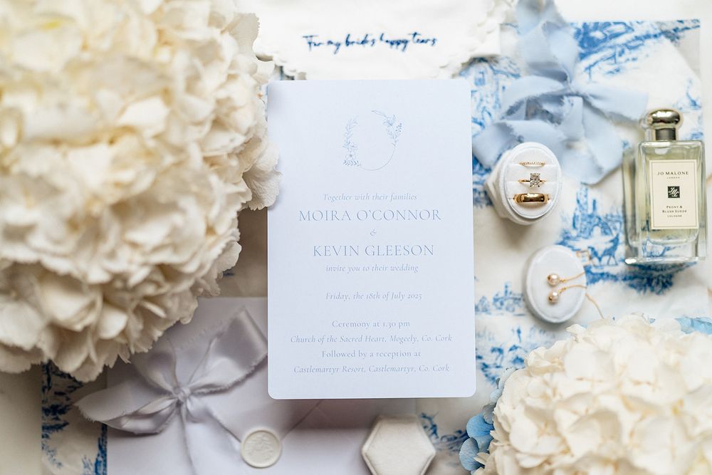 Elegant wedding stationery flatlay styled with delicate white flowers and blue silk ribbon on a light background.
