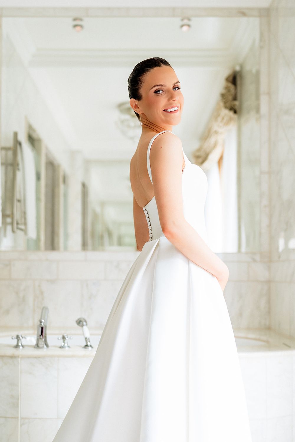 A beautiful white wedding dress with a fitted bodice and full skirt is showcased in an elegant marble bathroom setting.