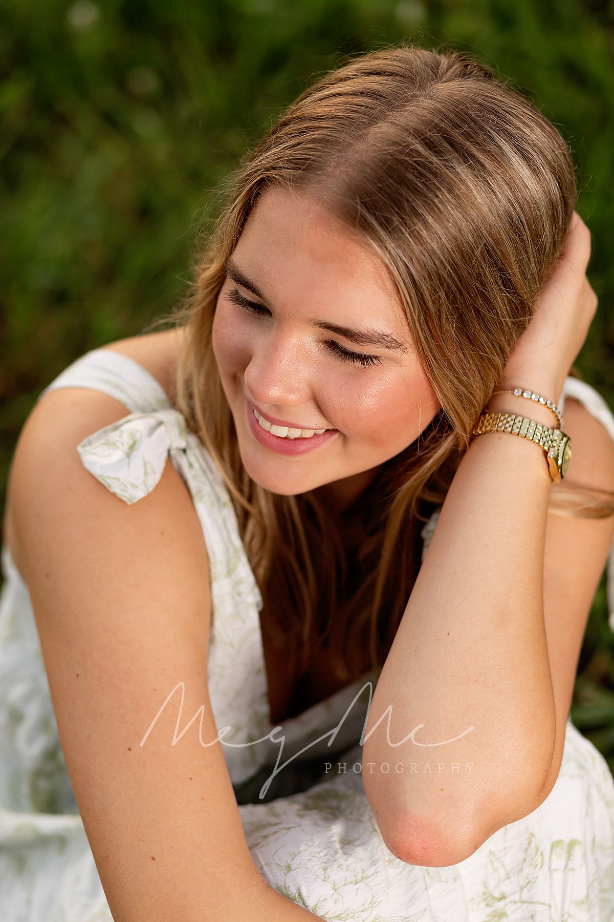 Natural portrait of teen wearing white dress and gold watch smiling while sitting outdoors. Senior Pictures by MegMc Photography, Medina, TN