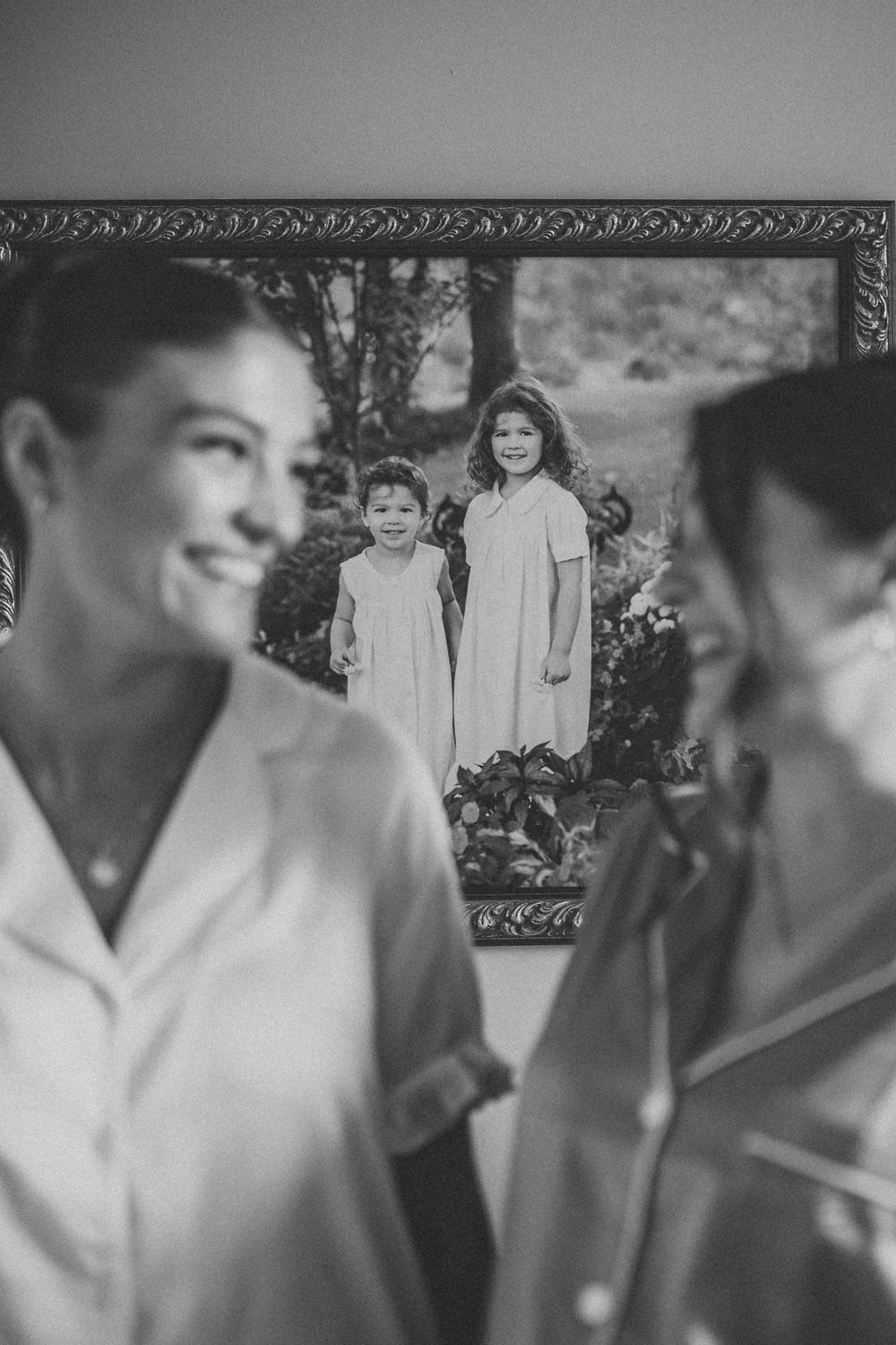 Black and white photo showing people in white clothing with a framed vintage photograph visible on the wall behind them.