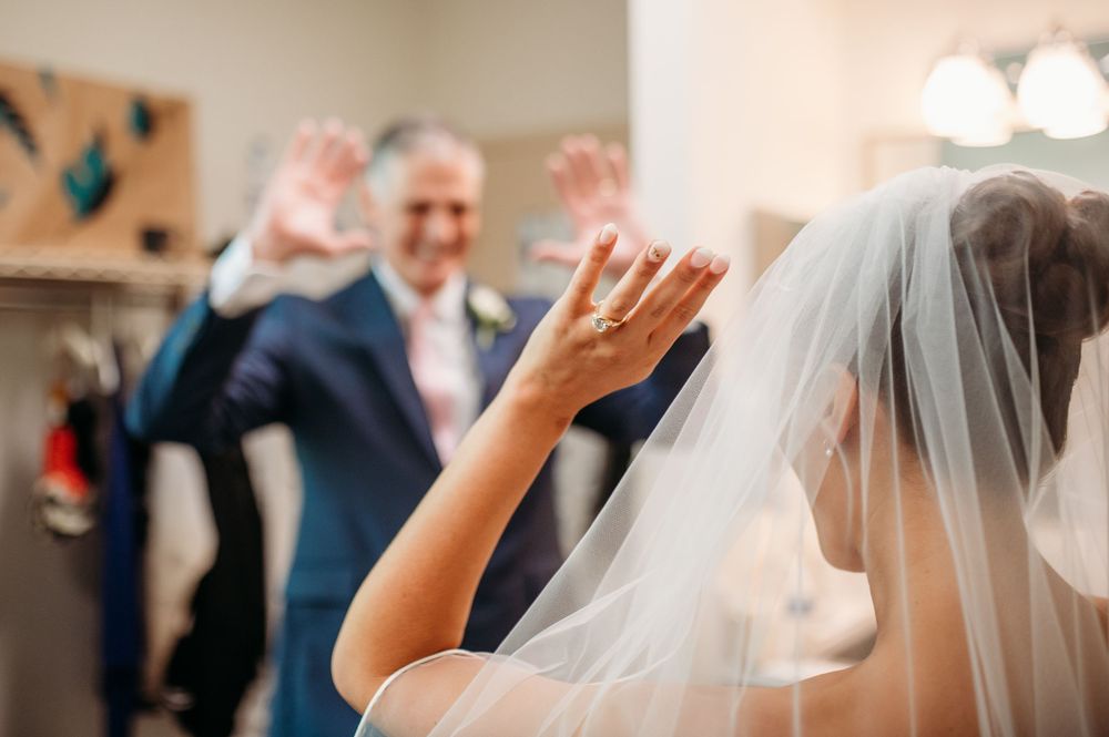 A bride in a white veil waves while celebrating during a joyful wedding reception moment.