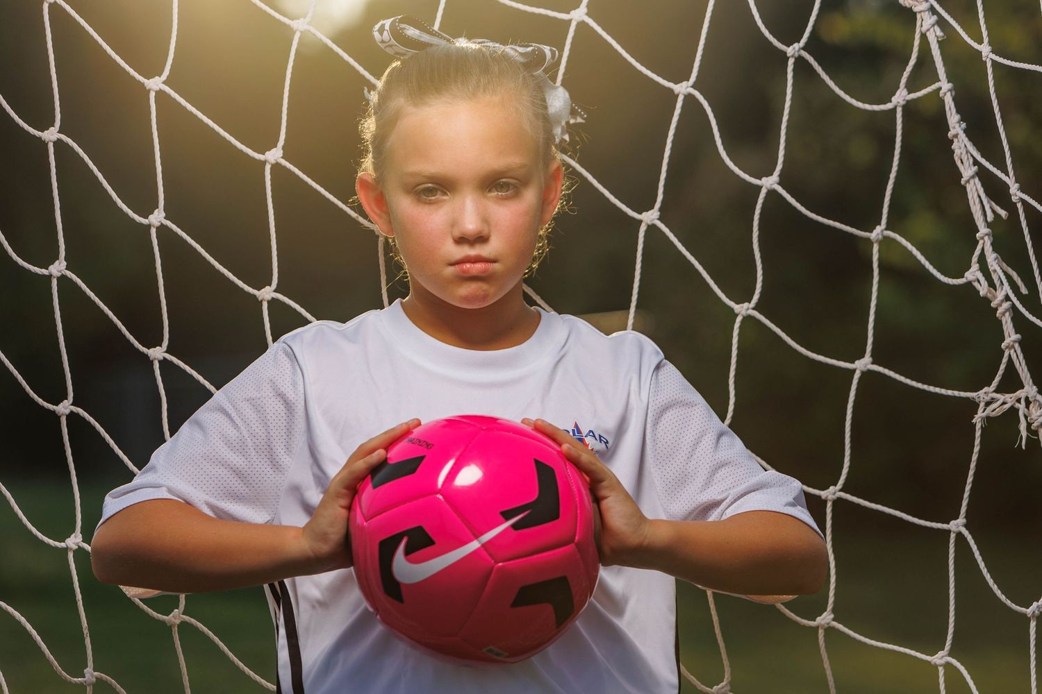 Youth athlete poses with pink soccer ball against goal net background.