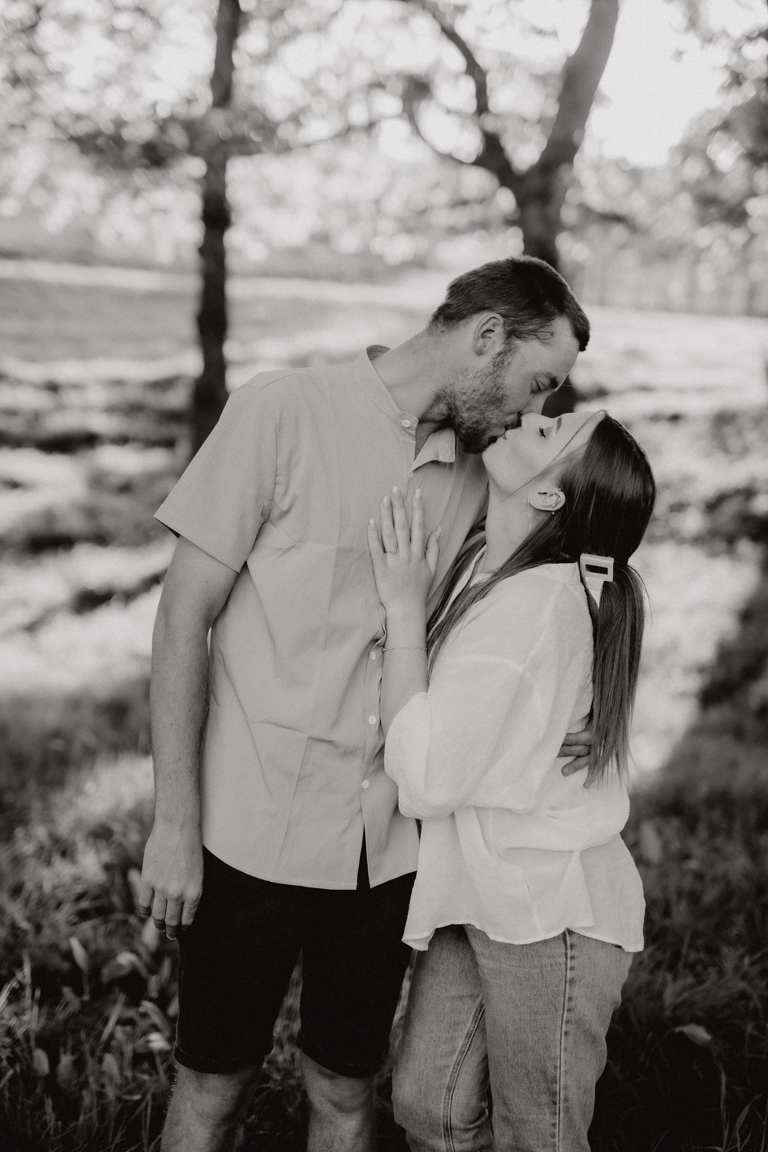 A romantic black and white photo of a couple sharing an intimate moment in a natural outdoor setting.