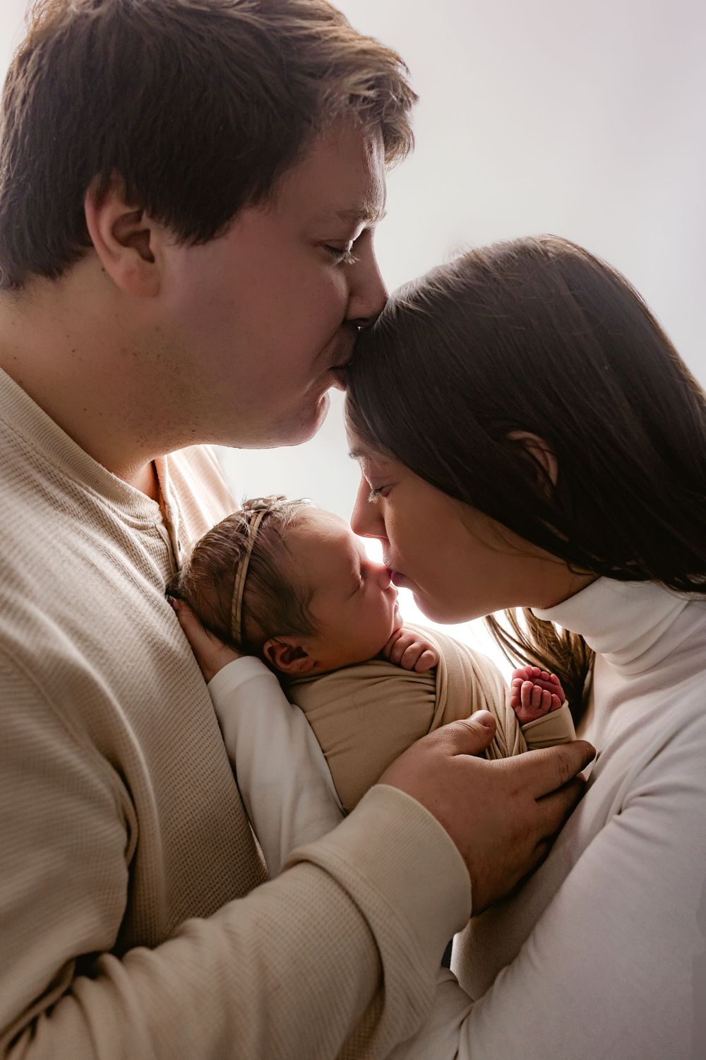 A loving couple embraces their newborn baby in warm light, creating an intimate family moment.