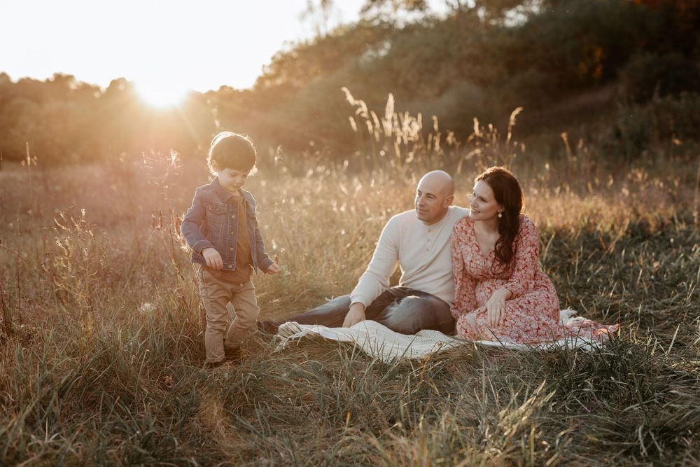A family relaxes together on a blanket in a sunlit meadow during golden hour as tall grass sways in the breeze.