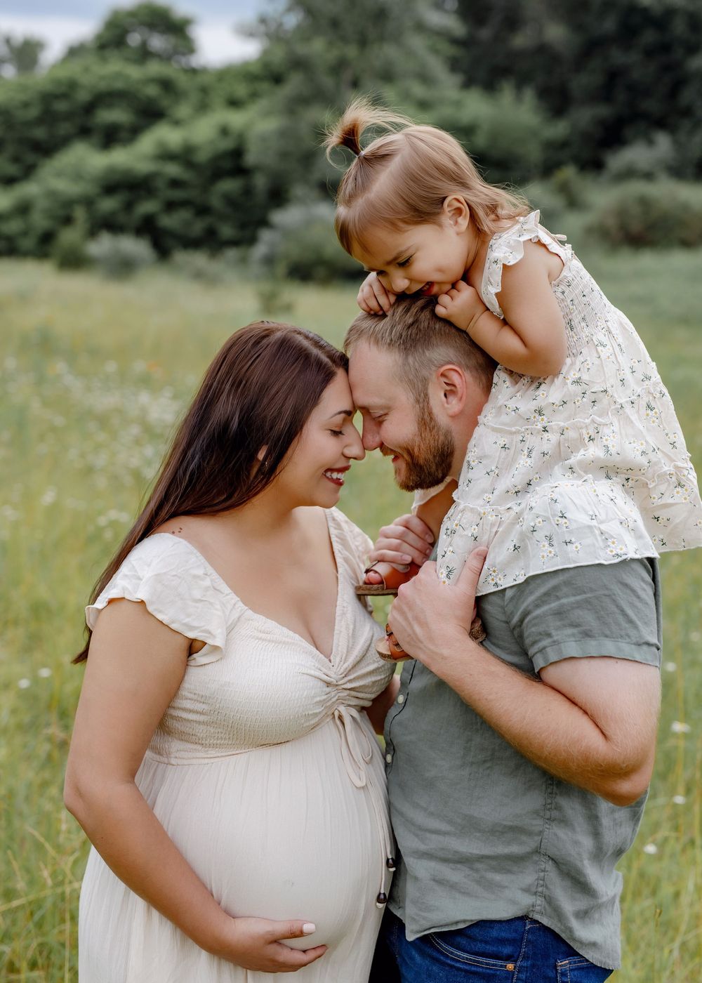 A loving family moment captured in a sunny meadow with white lace dresses and casual attire.