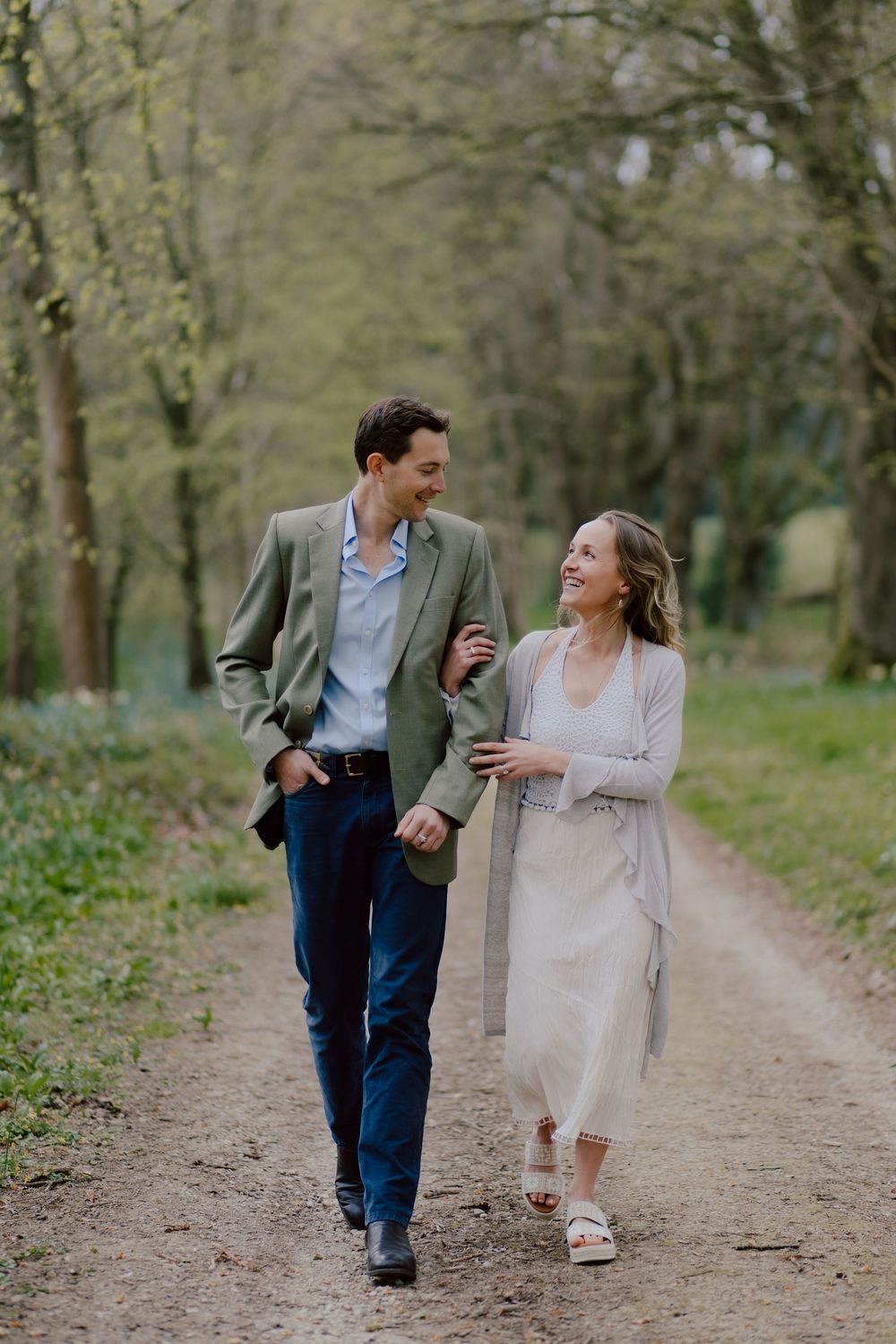 A couple walking and laughing together on a dirt path through a park on a spring day.