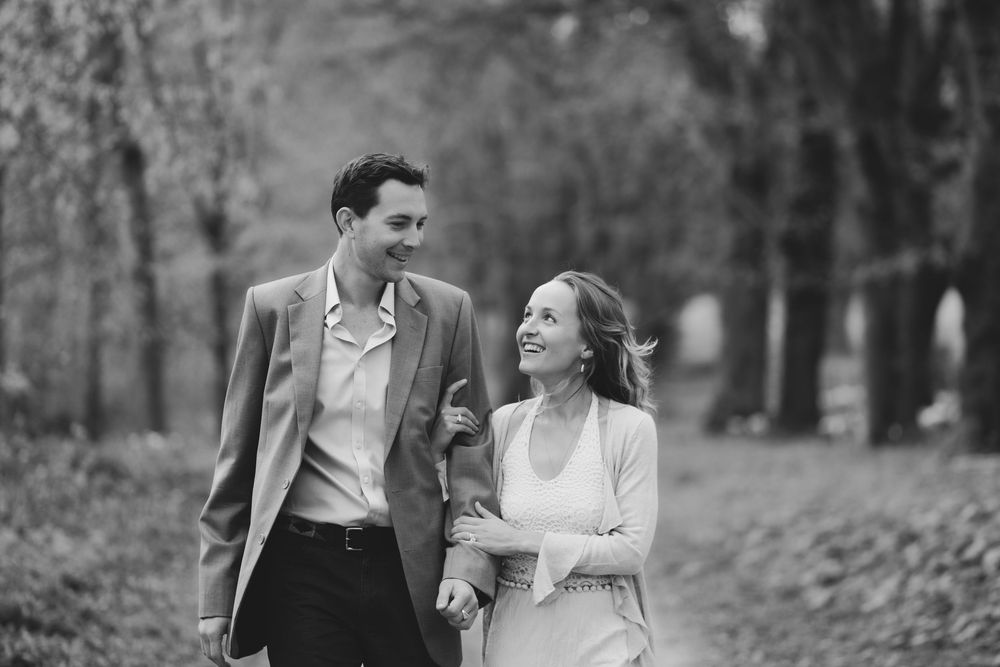A romantic black and white photo of a couple walking and laughing together in a tree-lined path.