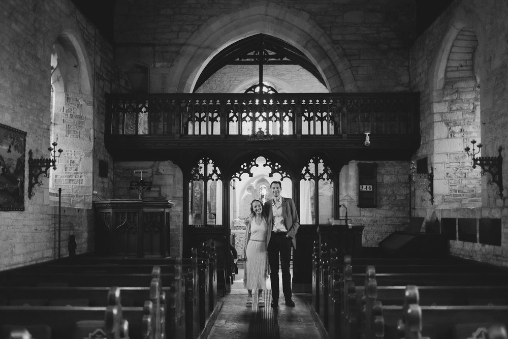A black and white photograph showing a church aisle with Gothic arches and pews leading to an altar.