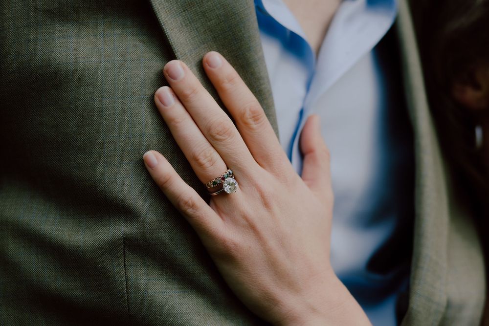 A close-up shot of a hand wearing an elegant engagement ring against a green and blue background.