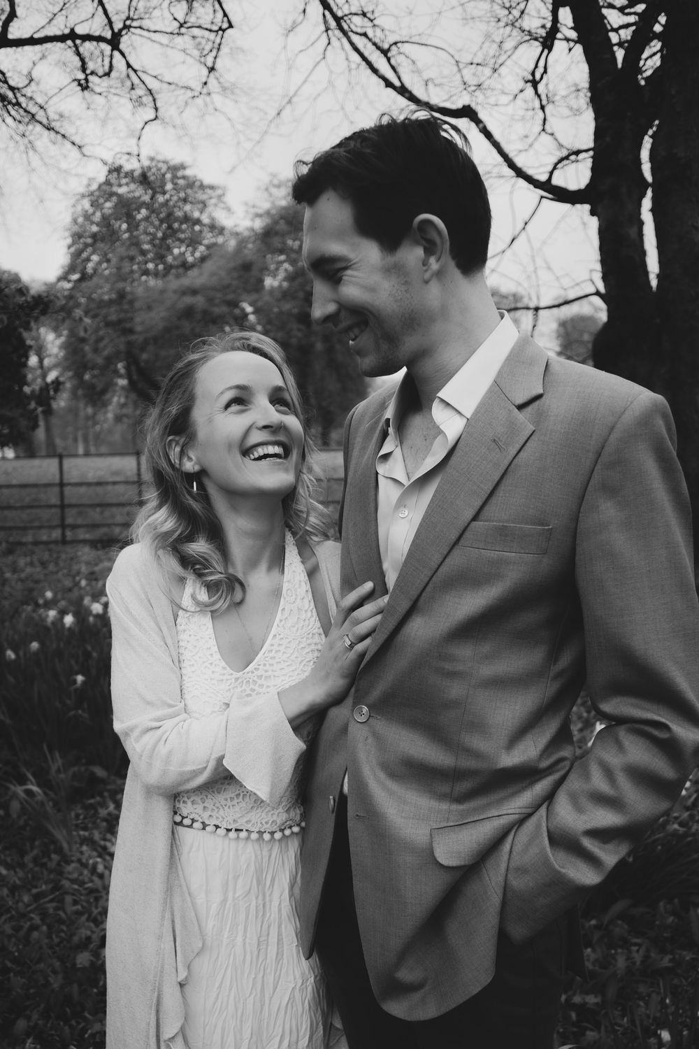 A romantic black and white portrait of a couple laughing together outdoors wearing elegant attire.