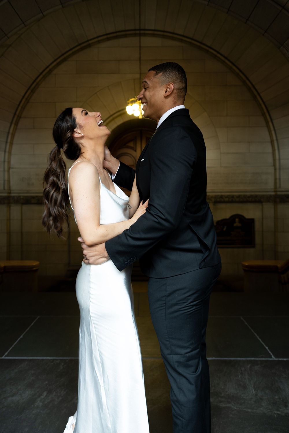A romantic wedding couple sharing an intimate moment under an arched stone passageway.