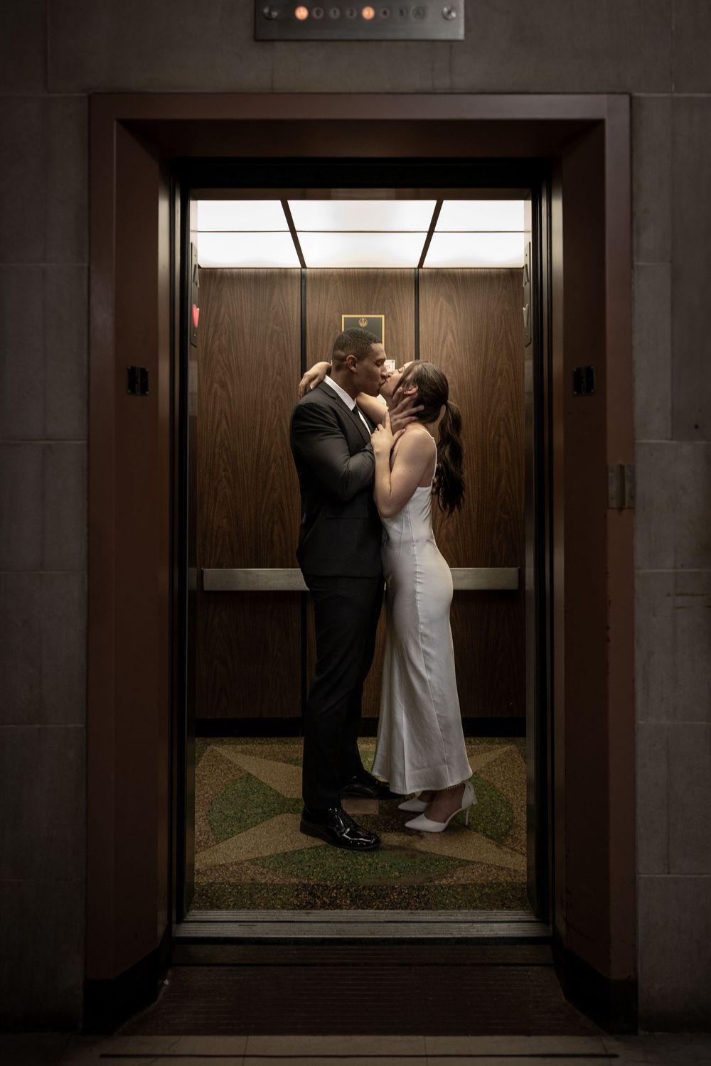A tender moment captured in an elevator with wood paneling and green patterned carpet.