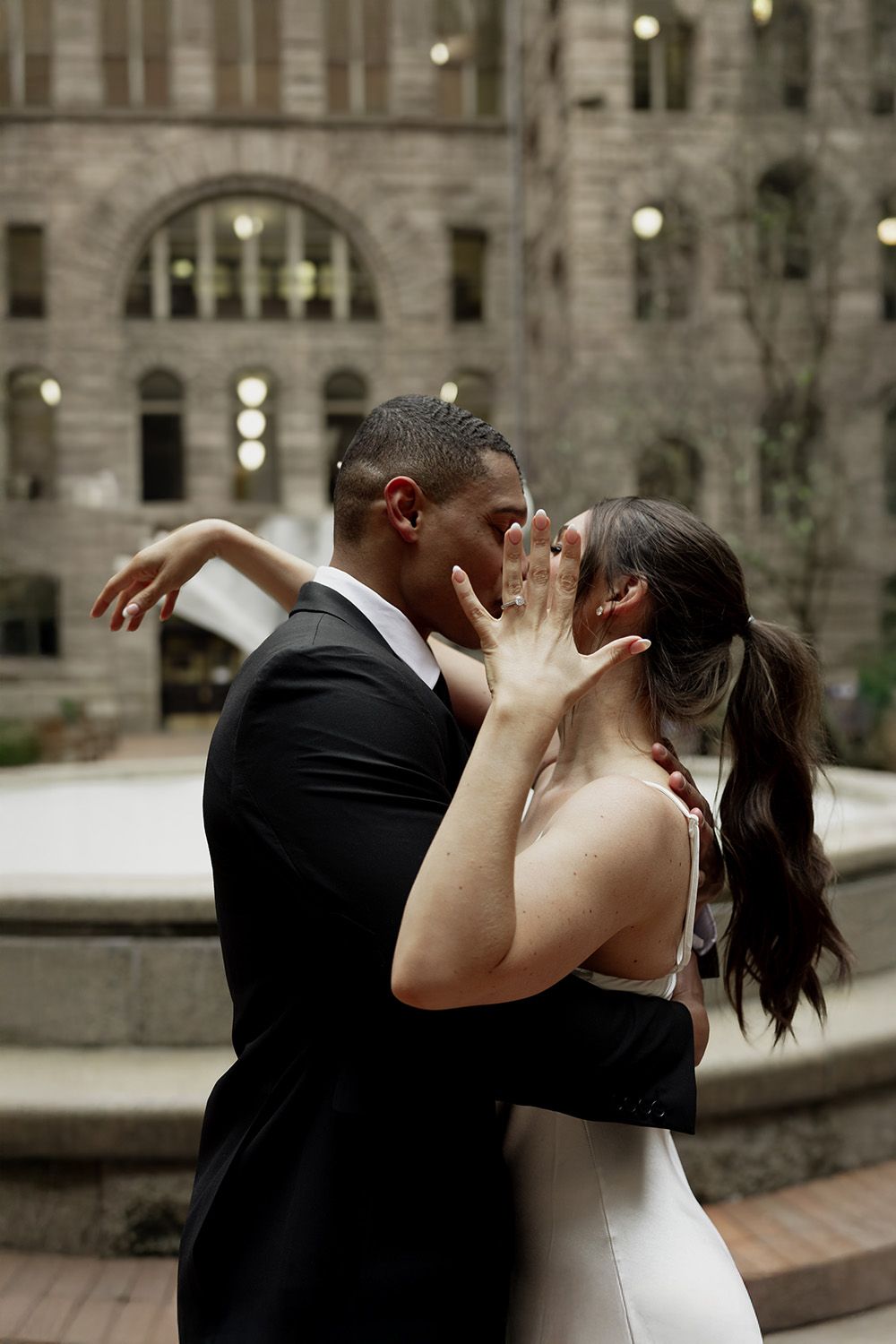 A romantic wedding moment as a couple embraces in front of an elegant stone building with glowing windows at dusk.