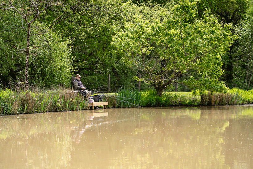 Man fishing at a big lake surrounded by trees in Devon