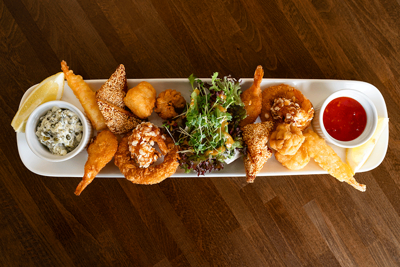 Seafood starter on rectangle plate with dips either end. Placed on dark wooden table.
