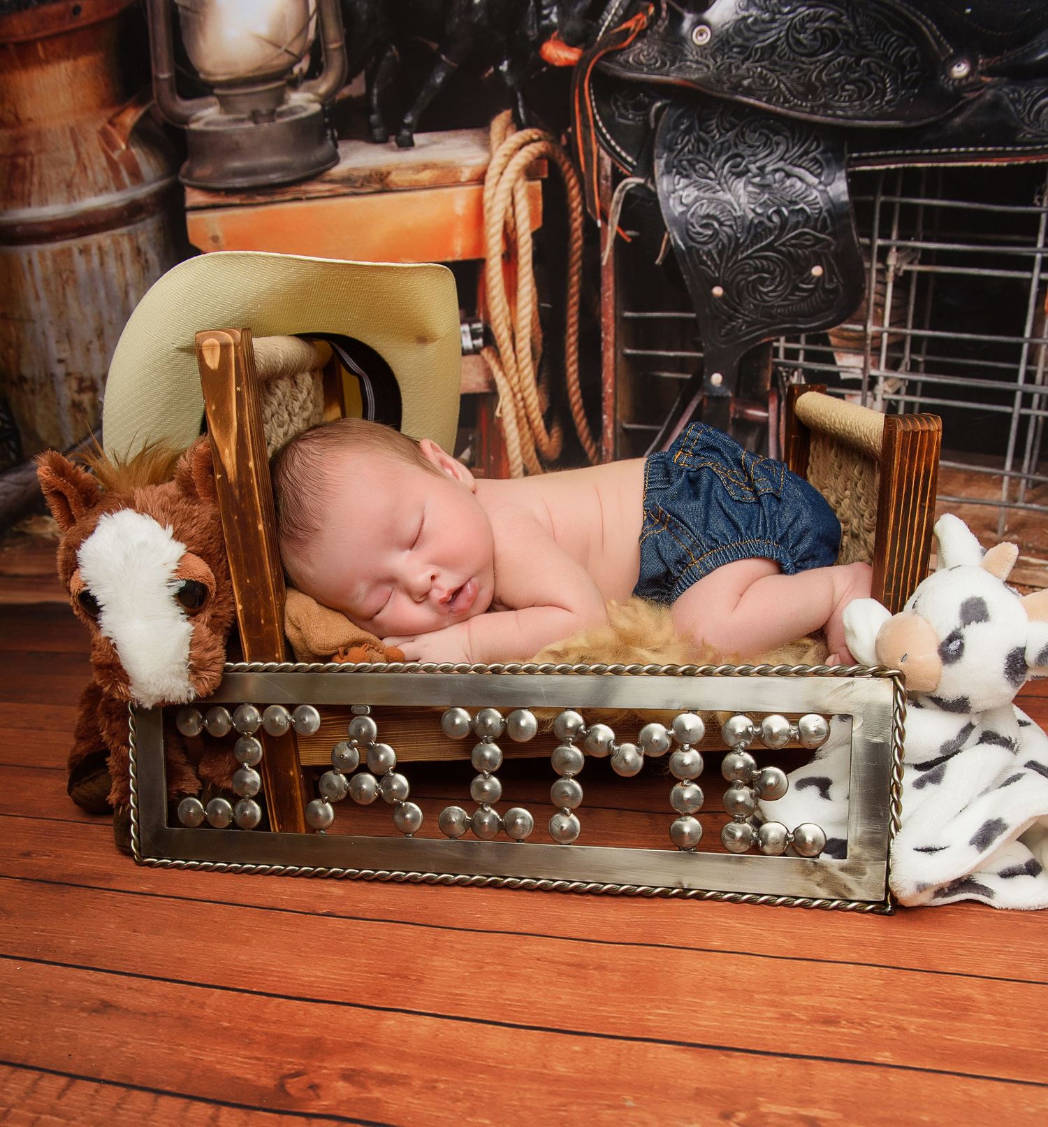 Rustic antique wooden box with soft blanket and stuffed animals staged as newborn photography prop on wooden floor.