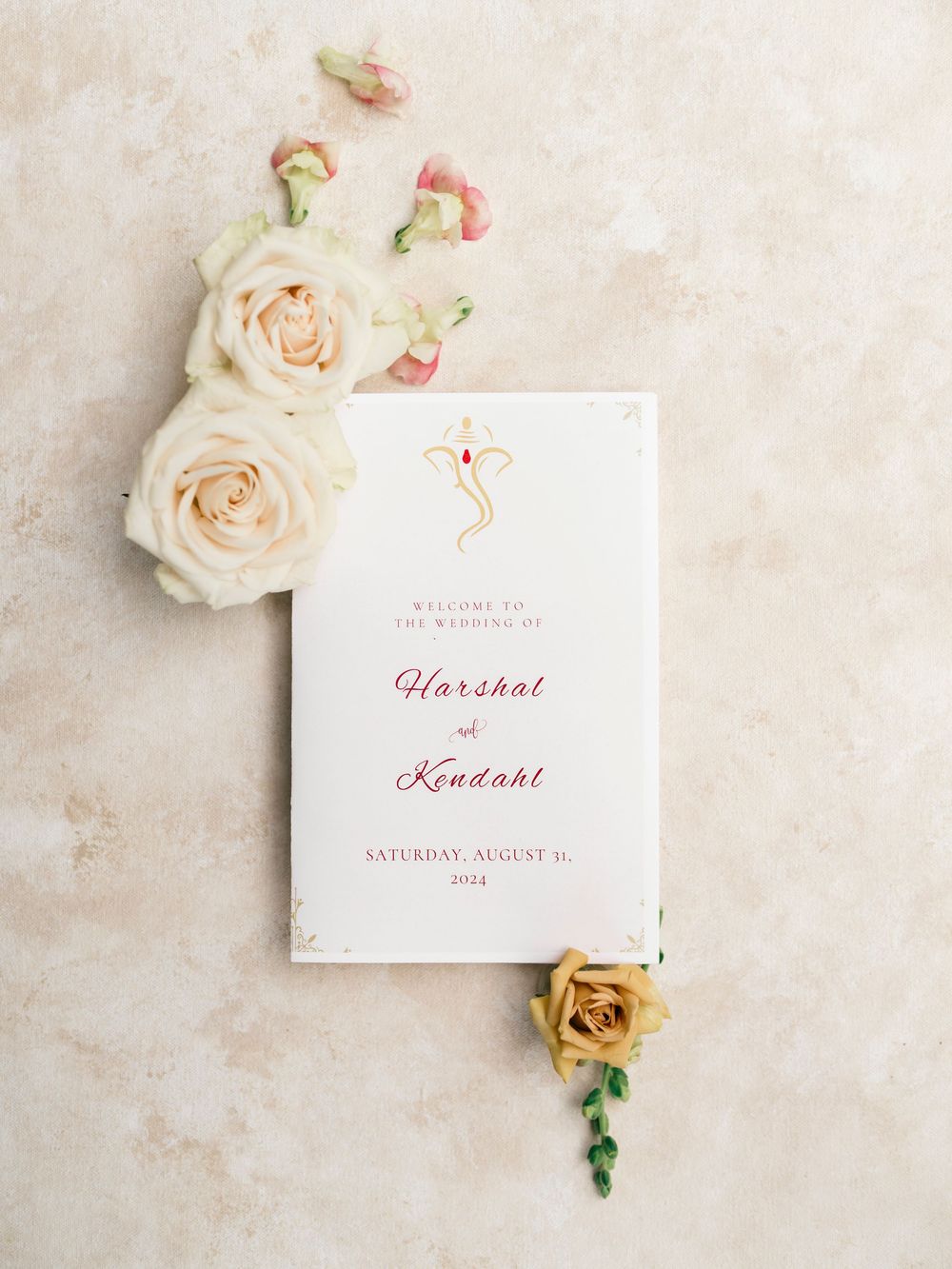 Elegant wedding invitation card with pink text and cream roses on a neutral textured background.