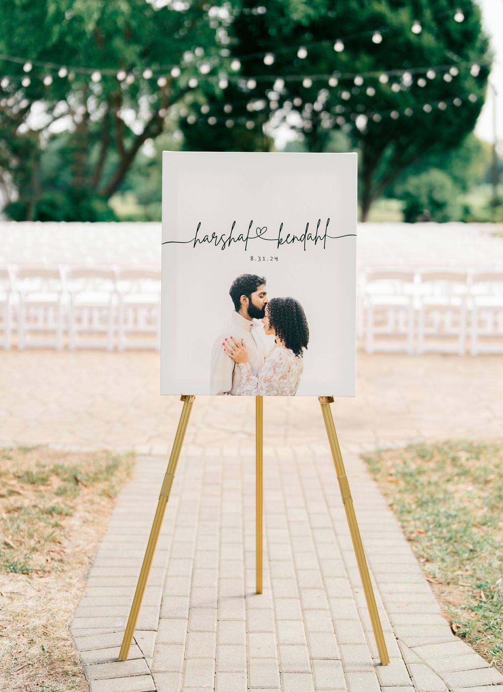 A wedding welcome sign on a gold easel features a couple's photo and calligraphy text with string lights in the background.