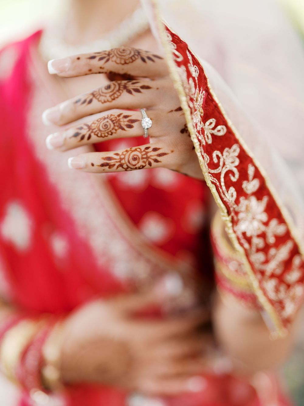 Detailed henna mehndi designs on hand with traditional red embroidered fabric in Indian wedding attire.