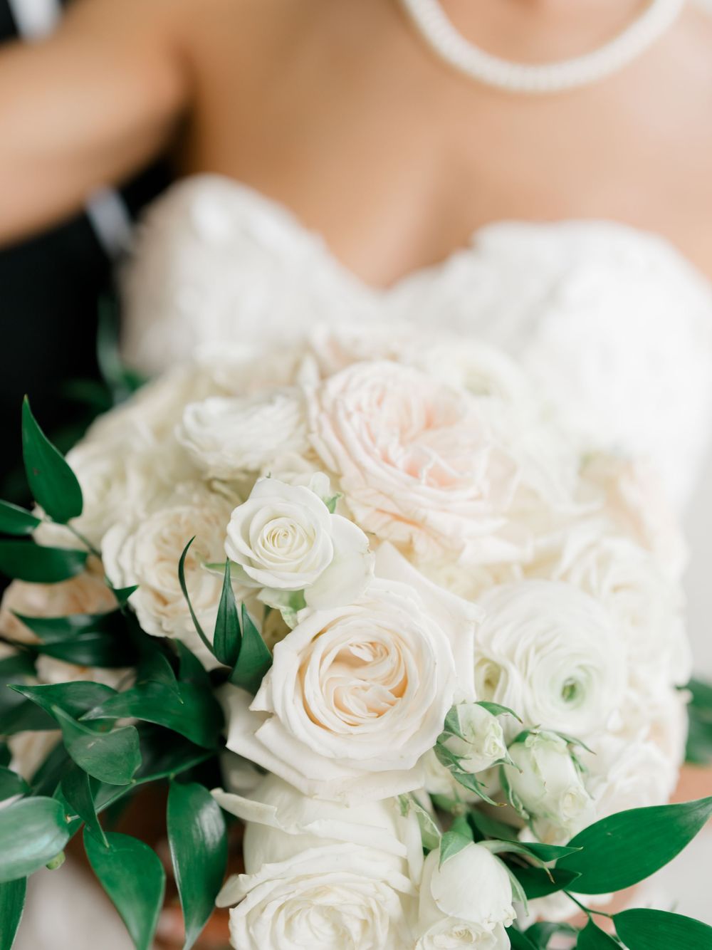Luxurious white and blush rose wedding bouquet with fresh green foliage against bridal gown.