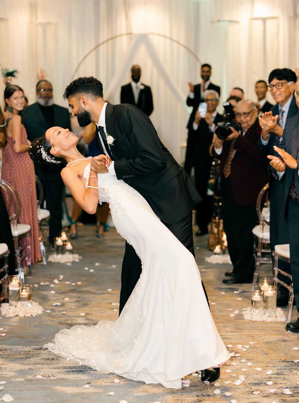 Newlyweds share romantic dip kiss during wedding ceremony surrounded by guests.