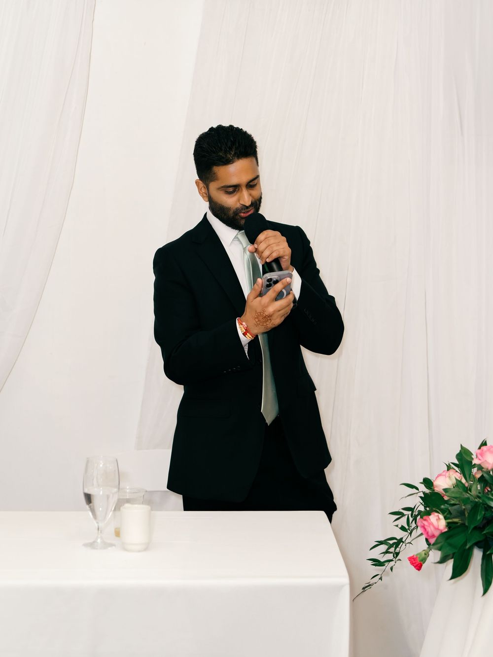 Wedding guest in black suit delivering speech at reception with floral decorations.
