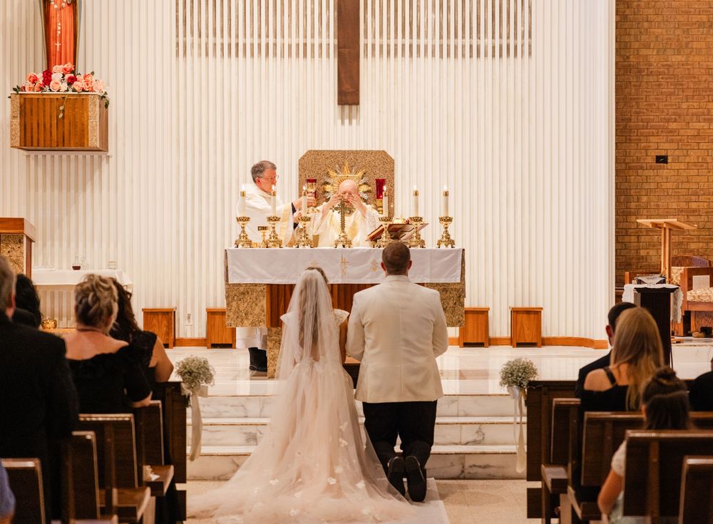 A wedding ceremony takes place inside a modern church with white walls and brick accents at the altar.