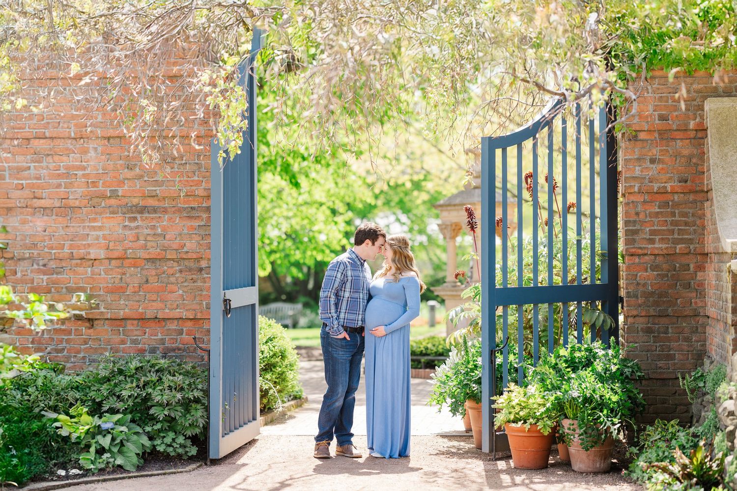 A couple stands in a romantic garden setting near an open blue gate surrounded by brick walls and greenery at Chicago Botanic Garden