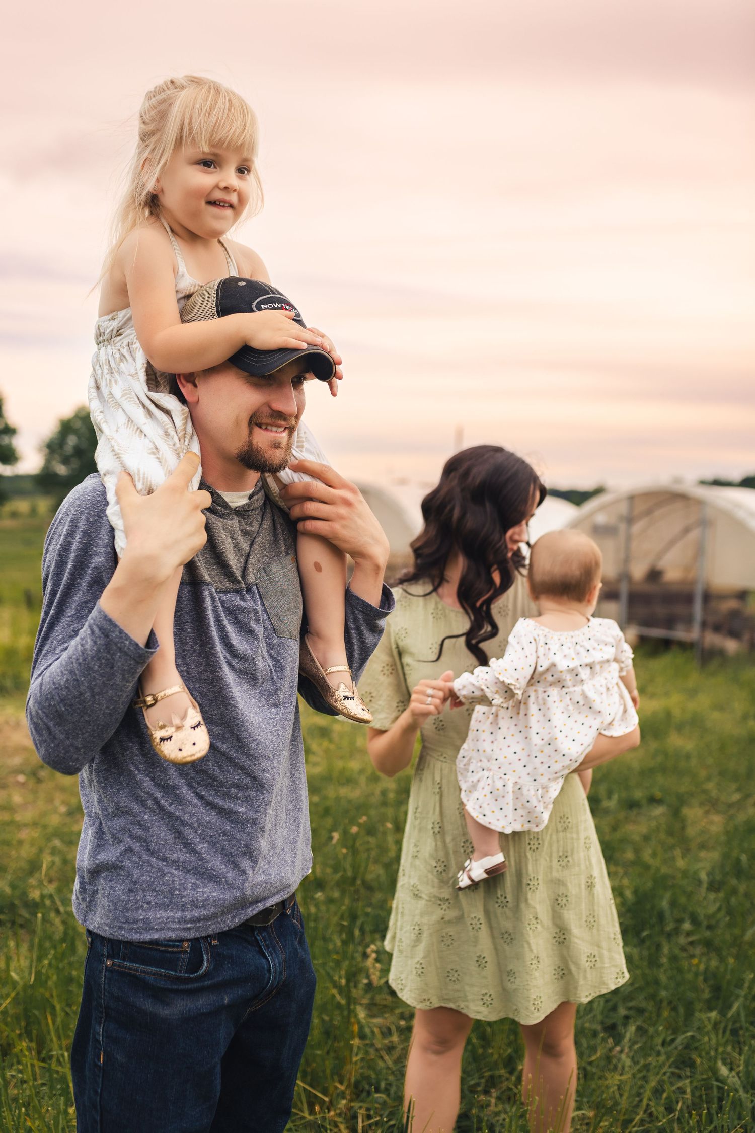 Family spending time together outdoors at sunset in a grassy field near a greenhouse.