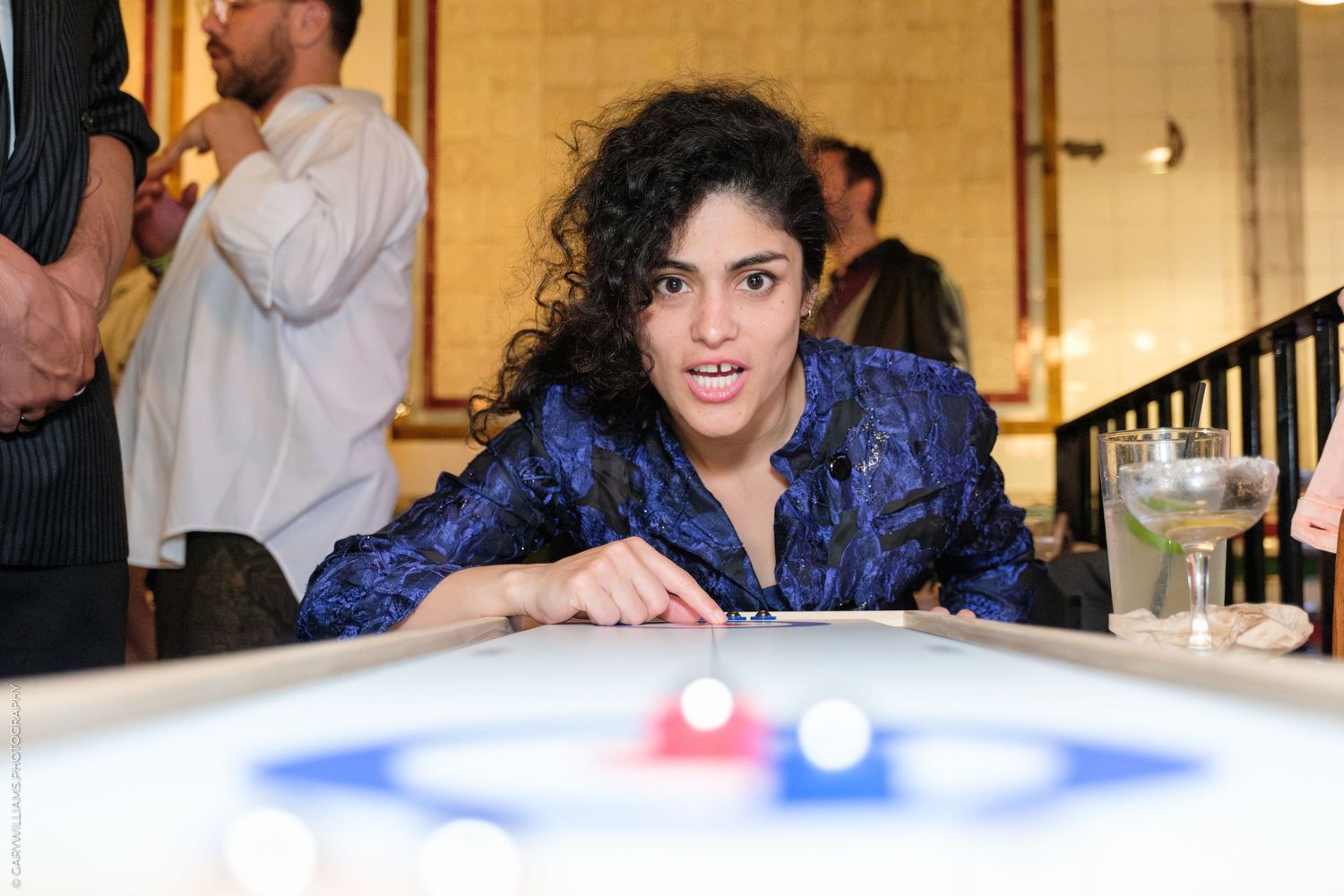 Someone in a blue sequined jacket leans over a billiards table during a game at an indoor venue.