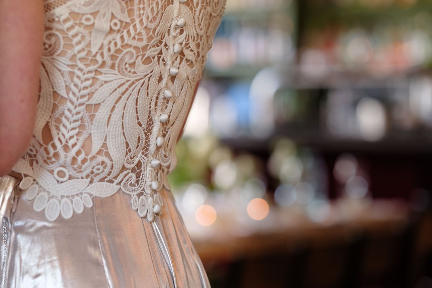 Intricate white lace detail on the bodice of a wedding dress shown in soft focus with blurred background.