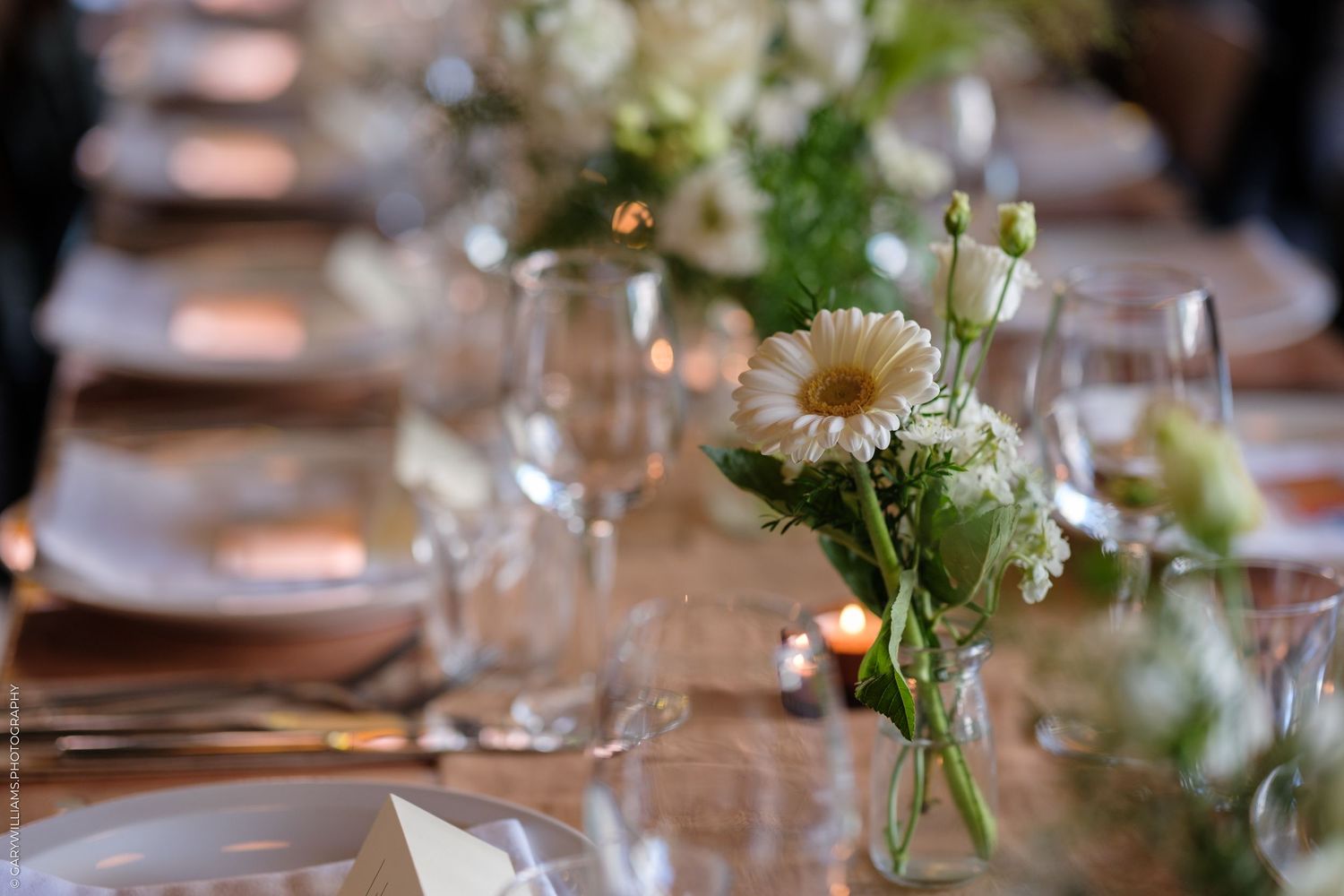 A delicate table setting with white daisy flower centerpiece and wine glasses for an elegant dinner party.