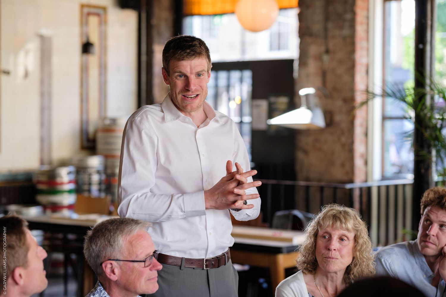 Someone in a white shirt gives a heartfelt speech at a restaurant gathering while guests listen attentively.