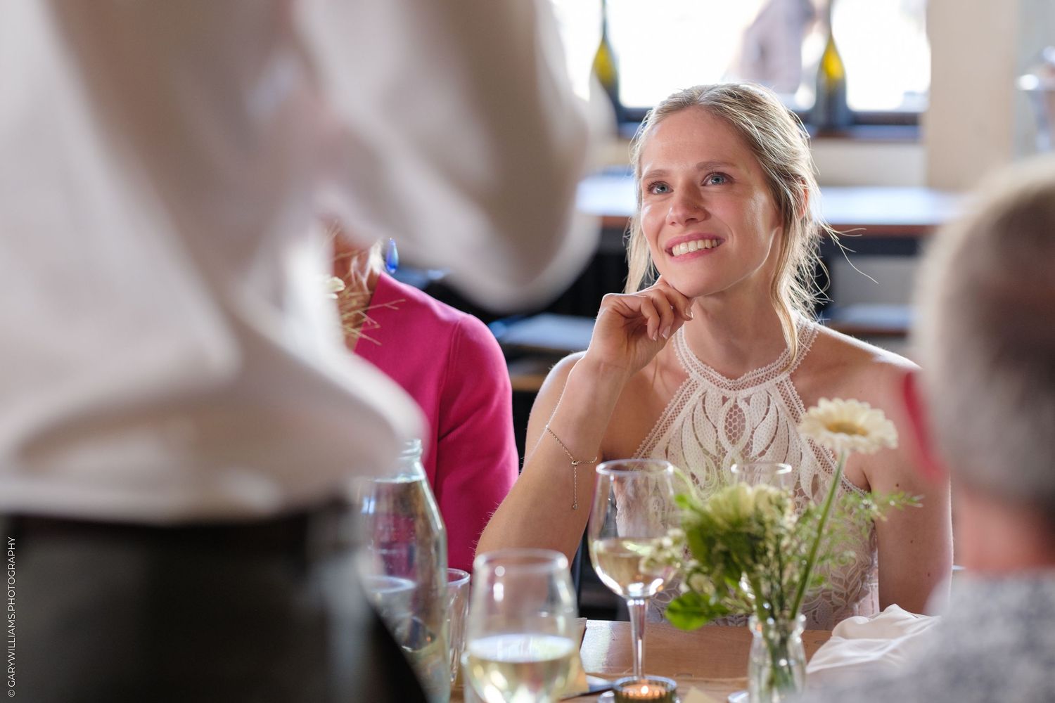 Guest enjoying wine and conversation at an elegant dinner table with white linens and floral centerpieces.