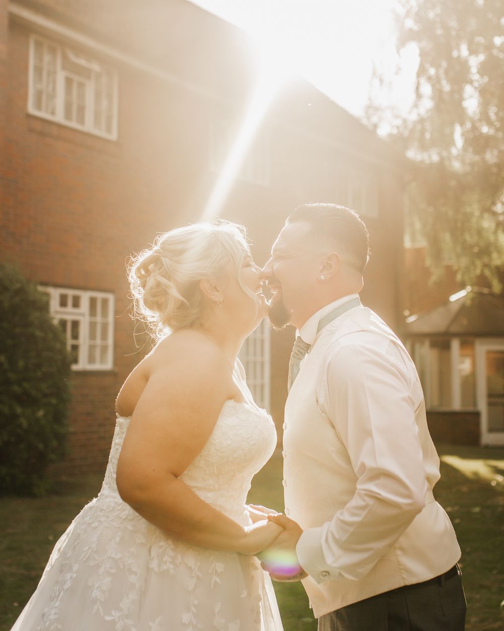 A romantic golden sunlit moment between newlyweds in front of a brick house.