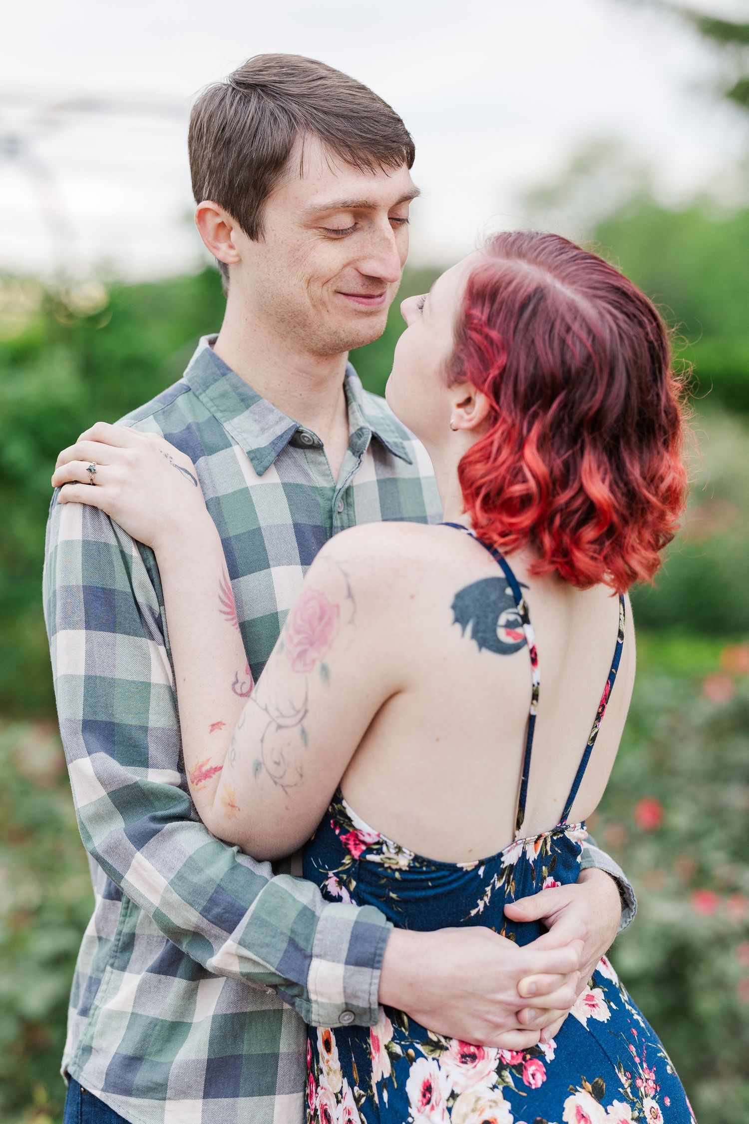 A couple embraces outdoors, with one wearing a plaid shirt and the other in a floral dress with bright red hair at Cantigny Park