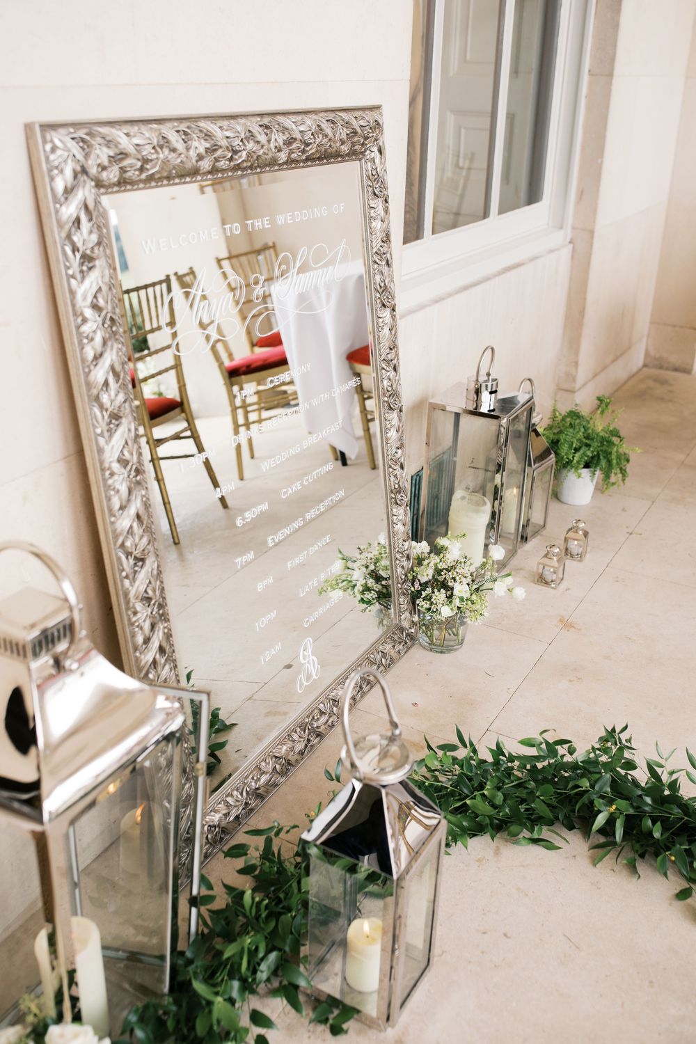 Elegant wedding decor displays feature ornate silver-framed mirrors and greenery arrangements along a light-colored wall.